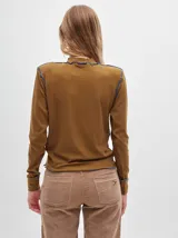 Polera de manga larga confeccionada en tela rib color bordó, con cuello alto y hombreras. Presenta costuras a la vista con pespuntes en hilo de color contrastante en el cuello, puños, hombros y ruedo.