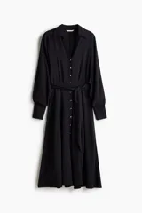 Vestido camisero midi negro de corte holgado, con cuello, escote en V y cierre frontal de botones dorados. Cuenta con mangas largas abullonadas con puños anchos y un lazo ajustable para atar en la cintura.