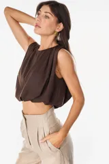 Top cropped satinado de color blanco, sin mangas, con hombros marcados y drapeado frontal.