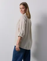 Camisa blanca de lino con cuello con solapa, manga larga regulable con presilla y botón, y abertura central con botones.