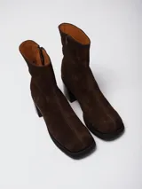 Bota de caña media con punta cuadrada, confeccionada en cuero gamuzado color marrón, con taco bloque y suela de goma negra.