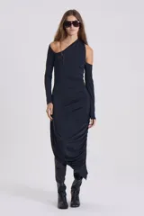 Vestido negro de silueta ajustada, largo midi, con un hombro descubierto y manga larga. Presenta drapeado en la falda y terminación irregular.