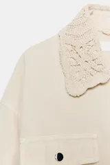 Chaqueta estilo safari color beige, con cuello de solapa tejido en crochet, manga larga, bolsillos delanteros con solapa y cintura ajustable con cordones. Cierre frontal con botones metálicos a presión.