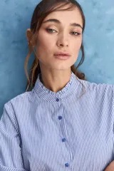 Camisa de rayas blancas y azules con cuello mao decorado con volados sutiles, cierre frontal de botones y mangas largas.