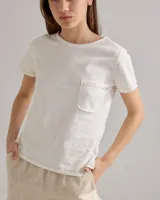 Remera blanca de algodón con cuello redondo, manga corta, bolsillo frontal y bordado en el pecho. Presenta costuras a la vista en color beige.