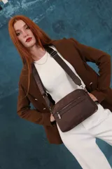 Bandolera de diseño moderno y funcional, confeccionada en nylon color marrón claro. Cuenta con múltiples compartimentos con cierre metálico, herrajes plateados y una correa ancha ajustable con detalle de marca.