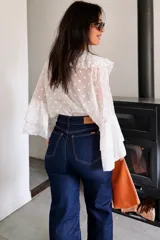 Blusa blanca con estampado de lunares, confeccionada en tela semitransparente. Presenta escote en V con volados frontales y mangas largas acampanadas con volados en los puños.