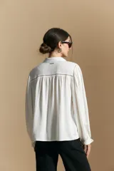 Camisa de manga larga color celeste, con cuello clásico, cierre frontal con botones y puños elastizados con volados. Presenta un diseño fluido con detalle de vainilla en la espalda.