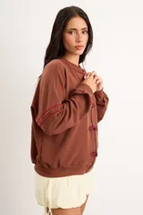 Campera oversize color crudo de algodón con spandex, corte de largo intermedio, mangas largas con detalles de costuras en zigzag bordadas y un gran diseño bordado a mano de una flor en la espalda.