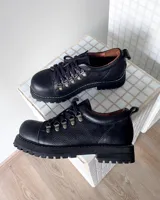 Zapatos tipo borceguíes bajos de cuero vacuno negro, con cordones y ganchos metálicos. Presentan suela track dentada y costuras visibles en el borde de la suela.
