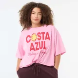 Camiseta oversize de manga corta color rosado, con cuello redondo y estampa frontal con la leyenda "Costa Azul" en rojo y amarillo.