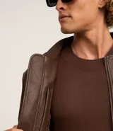 Campera estilo bomber de hombre, color marrón oscuro, confeccionada en poliuretano (PU) con cuello alto, cierre frontal y puños y bajo acanalados.