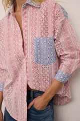 Camisa de corte oversized confeccionada en broderie de algodón con diseño combinado. Presenta un estampado de rayas verticales en tonos rojos y blancos, con detalles en contraste de color azul en el cuello, los puños y el bolsillo frontal. Posee cierre frontal con botones y mangas largas.
