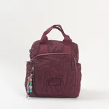 Mochila de diseño acolchado en color bordó, con costuras decorativas que forman letras. Cuenta con un compartimento principal con cierre, un bolsillo frontal con cierre, asas superiores de mano y correas ajustables. Incluye un colgante decorativo con cuentas en el cierre frontal.
