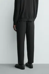 Pantalón de corte regular fit, color negro, confeccionado en tejido elástico. Presenta cintura elástica, cierre frontal con cremallera y botón, bolsillos laterales y bolsillos traseros de vivo.