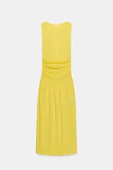 Vestido largo amarillo de algodón, con cuello barco y mangas sisa. Presenta diseño drapeado en los laterales y falda de corte evasé con volumen en el bajo.