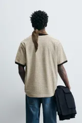 Camiseta de corte regular con cuello redondo y mangas cortas. Diseño a rayas horizontales en color crema y negro. Acabados con rib a contraste en cuello y mangas.