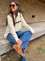 Sweater de tejido de punto en color beige, con corte holgado y diseño de cuello redondo. Presenta apliques decorativos de cuero en la parte frontal superior, formando un detalle geométrico.