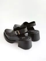 Zapato tipo slingback color negro, con plataforma y taco cuadrado. Presenta una puntera cuadrada y cierre con hebilla metálica en la tira trasera.