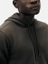 Buzo con capucha de corte clásico, confeccionado en tejido de algodón, con bolsillo frontal tipo canguro y puños acanalados.