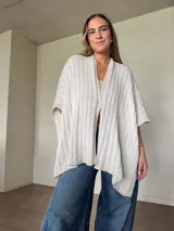 Ruana tejida de algodón con hilo lurex en punto jersey, color azul, con diseño amplio y detalle de etiqueta de cuerina en la parte posterior.