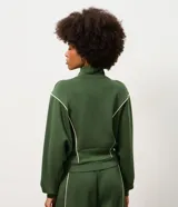 Campera deportiva de microfibra color verde oscuro, con cuello alto, manga larga y cierre frontal. Presenta recortes estructurados con vivos contrastantes claros, barra ajustada y puños alargados.