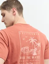 Remera verde con estampado en la espalda de una playa con palmeras y la frase "Ride the waves".