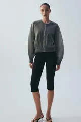 Chaqueta estilo bomber de punto color beige con acabado brillante, cuello redondo, manga larga con puños elásticos y cierre frontal con cremallera.