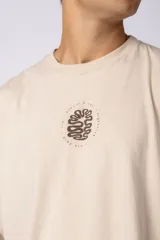 Remera oversize de corte holgado, color blanco, con cuello redondo y mangas cortas. Presenta un pequeño estampado circular en el centro del pecho con un diseño abstracto inspirado en arrecifes.