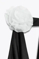 Body negro de cuello halter con escote drapeado pronunciado, detalle de flor blanca en relieve y espalda descubierta.