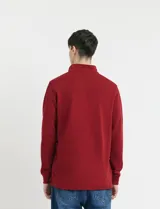 Remera de manga larga con cuello polo, confeccionada en tejido de punto canalé francés. Presenta abotonadura frontal con botones de madera y detalles a contratono en la cartera y el interior del cuello.