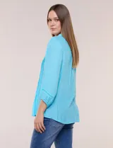 Blusa celeste de silueta suelta y textura liviana, con escote en V, cuello mao y cierre frontal de botones. Cuenta con alforzas verticales en el pecho y mangas tres cuartos con puños elastizados y detalle de galón calado.