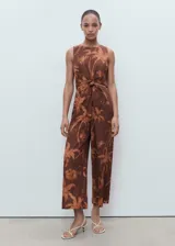 Mono largo marrón con estampado de palmeras, diseño sin mangas, cuello redondo, detalles cut-out en los laterales y un nudo decorativo en la parte delantera.
