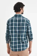 Camisa de manga larga con estampado de cuadros en tonos verde petróleo, blanco y líneas finas en color ocre. Presenta cuello clásico con botones y puños con detalle en contraste.