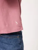 Remera blanca de manga corta con vuelta en los puños y detalle de botón dorado. Presenta cuello redondo y corte recto.
