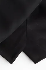 Short pollera de tiro alto negro con sutiles rayas verticales, diseño cruzado al frente y detalle de tira lateral con hebilla.