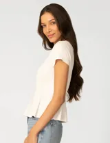 Remera blanca de manga corta con cuello redondo, confeccionada en una mezcla de modal, poliéster y elastano. Presenta un diseño con alforzas verticales en el frente que aportan estructura y una silueta relajada.