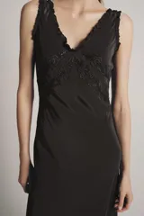 Vestido largo de viscosa en color negro, con escote redondo y tirantes anchos con detalle de volados. Presenta bordados florales a tono en la parte superior y bajo con terminación evasé.