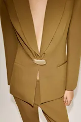 Blazer entallada color tostado con cuello solapa, manga larga y hombreras. Presenta cierre frontal con un botón metálico dorado y bolsillos delanteros de vivo.