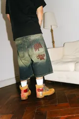 Bermuda de jean estilo baggy con lavado verde desgastado. Presenta grandes bolsillos traseros con bordados en hilo rojo que simulan caracteres chinos.