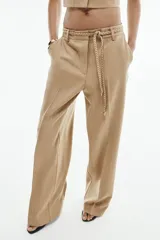 Pantalón de tiro medio color beige con sutiles rayas verticales blancas, de corte recto y amplio. Cuenta con bolsillos delanteros y un cinturón trenzado del mismo tejido con cordón ajustable.