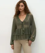 Blusa de tul transparente color verde oliva, con diseño de volados en el frente, escote en V con lazo y borlas decorativas, y mangas largas amplias con puños elásticos.