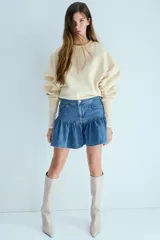 Pollera corta de denim de algodón rígido, con cintura estándar, cierre y botón, bolsillos delanteros y diseño acampanado con frunce.