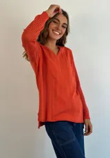 Buzo de tejido de punto ligero, color dorado con brillo sutil, escote en V y manga larga con diseño calado en los puños.