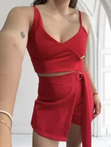 Conjunto de top y short pollera color rojo. El top es corto, con breteles finos y escote en V cruzado. El short es de corte sastrero con un lazo lateral.
