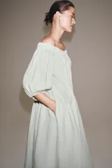 Vestido midi confeccionado en lino 100%, con escote recto elástico estilo hombros descubiertos, mangas abullonadas y detalle de pliegues en la cintura. Cuenta con bolsillos laterales ocultos y bajo asimétrico.