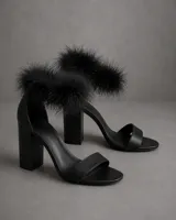 Sandalias de taco cuadrado alto, color negro, con tira delantera simple y detalle de plumas decorativas en la zona del tobillo.