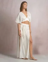 Pantalón palazzo de lino color blanco, de tiro alto con cintura elástica y cinto lazo con cuentas decorativas en las puntas. Presenta aberturas laterales pronunciadas en las piernas y corte amplio.