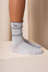 Medias blancas de caña media con tejido acanalado, detalles de volados negros en el puño y bordado con la palabra "Criado" en color negro.