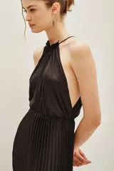 Vestido largo de color negro con diseño plisado en toda la falda. Presenta un escote halter con espalda descubierta y una cintura elástica que define la silueta.